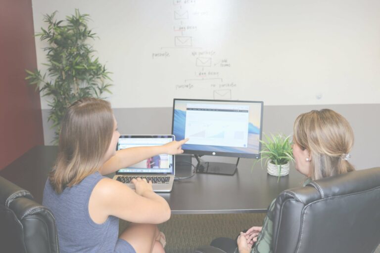 A web designer pointing at a screen while discussing web maintenance strategies with a client.