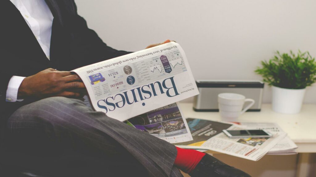 Professional in business attire reading Business newspaper at desk with coffee cup and digital devices
