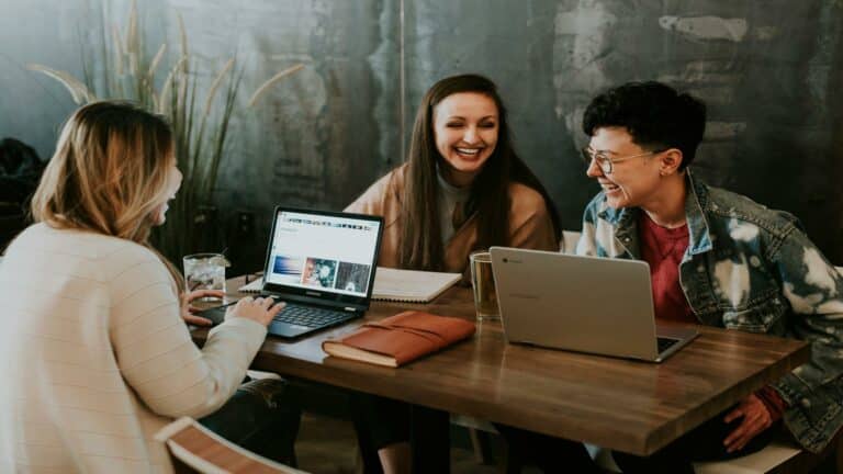 Three young professionals collaborating at a coffee shop with laptops, engaged in a casual business meeting