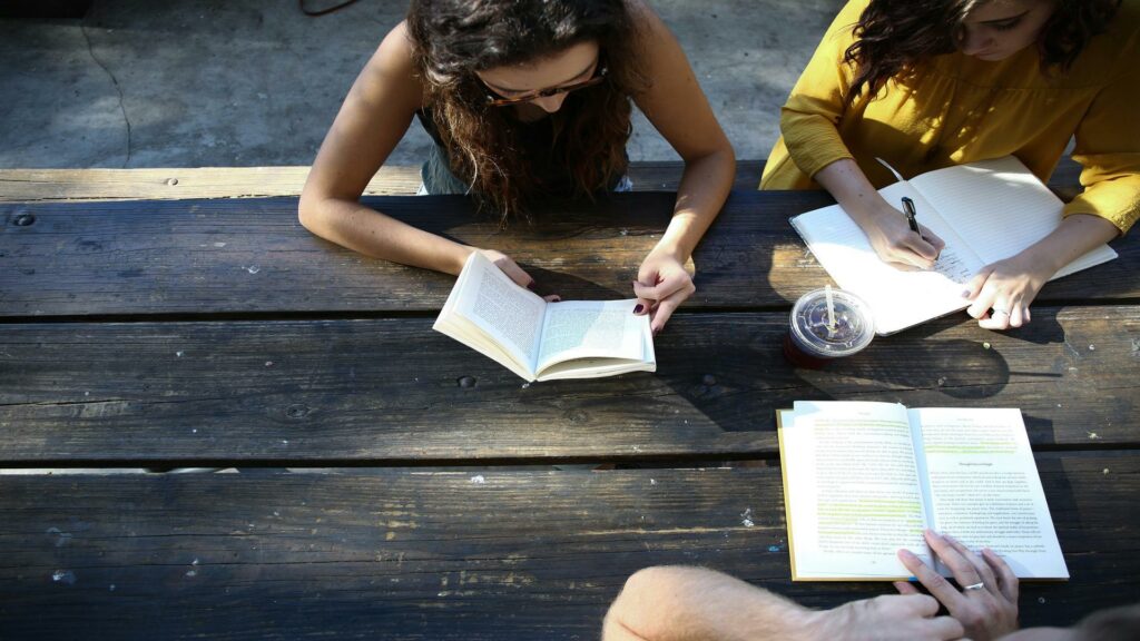 Group of people studying together at a wooden table outdoors.