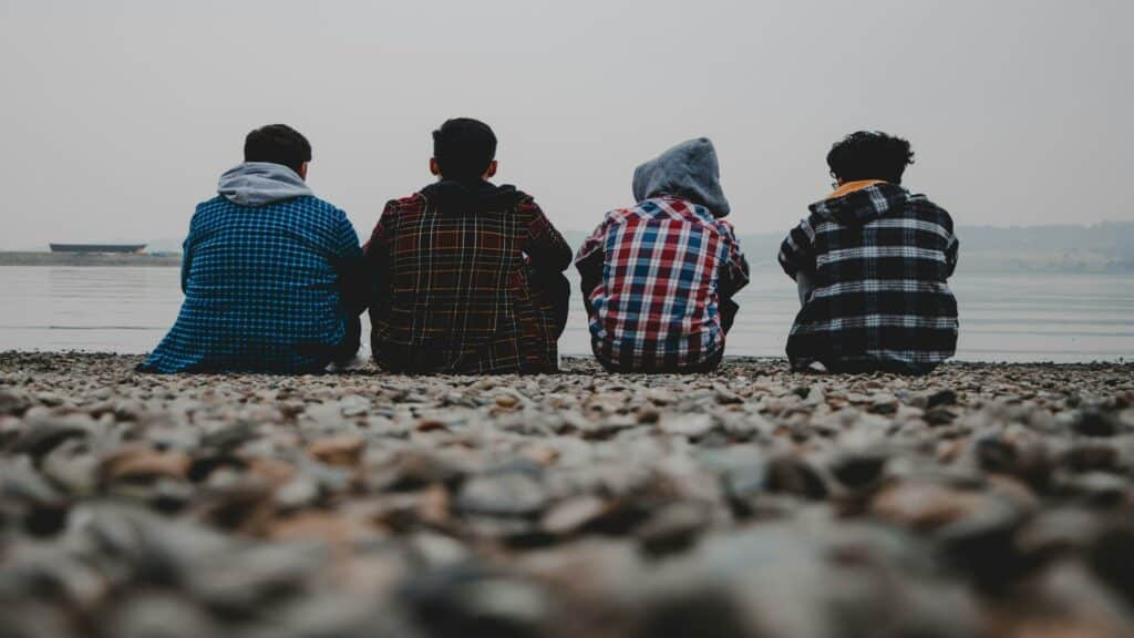 Four people sitting on a rocky shore facing a lake on a foggy day.