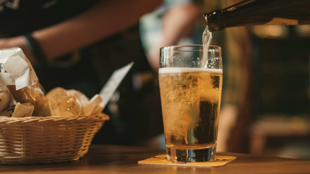 Golden beer being poured into a clear glass with bread basket in background