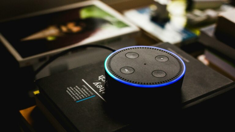 Amazon Echo device with blue light ring on black surface with scattered papers in background