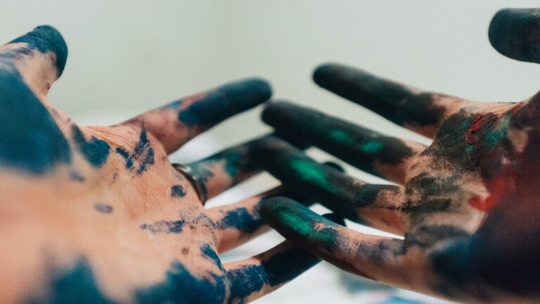 Close-up of hands covered in blue and green paint showing artistic commitment