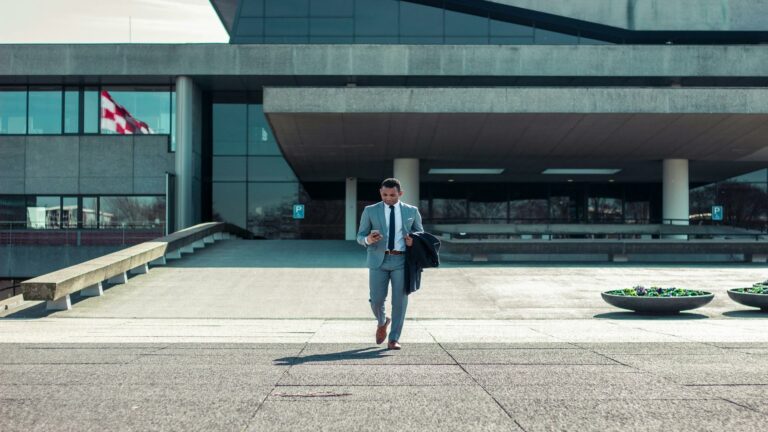 Professional in grey suit checking mobile device outside modern office building