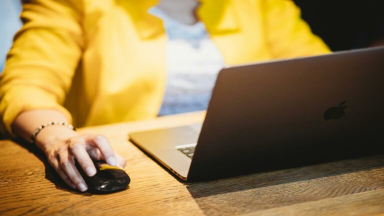 Person in yellow sweater using MacBook and mouse on wooden desk