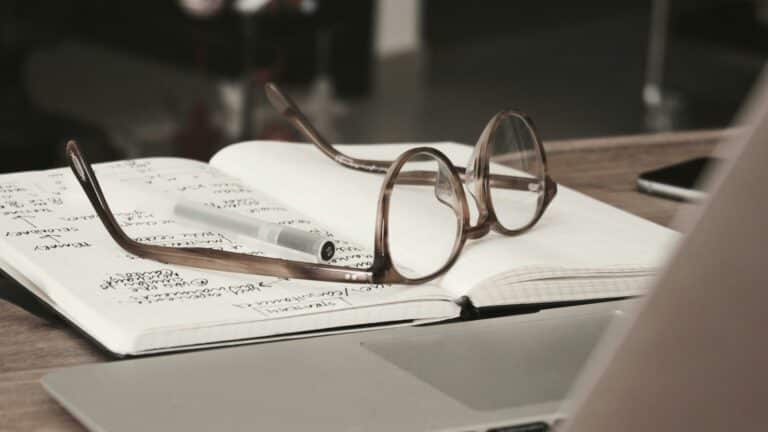 Eyeglasses resting on an open notebook with handwritten notes, symbolizing planning and research.