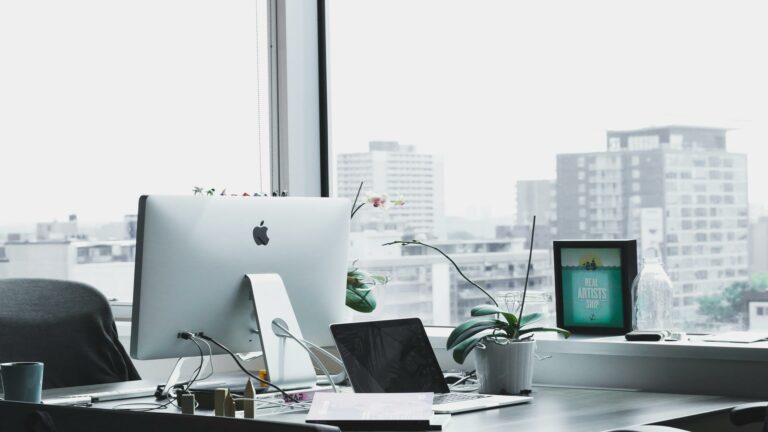 Office desk with computers and a view of city buildings