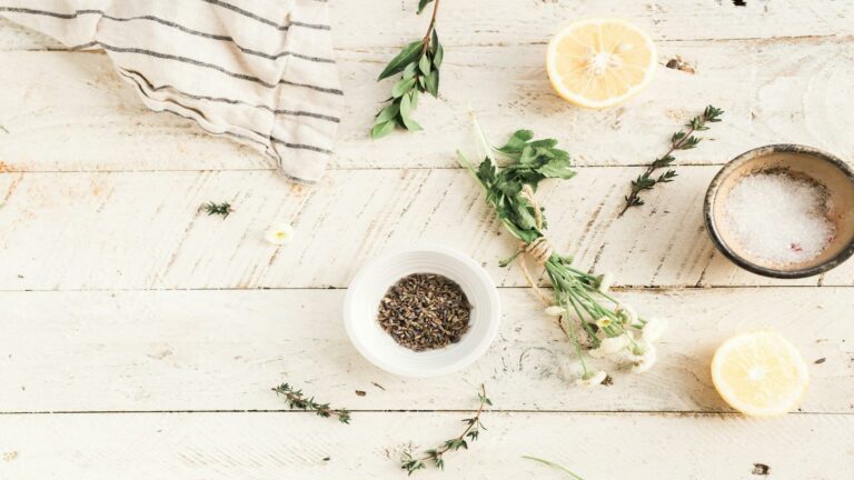 Flat lay of herbs, lemon halves, and spices on a rustic wooden surface.