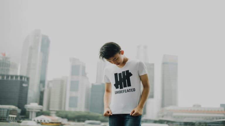 Young man wearing a white t-shirt with 'Undefeated' logo in front of a cityscape, representing online marketing solutions