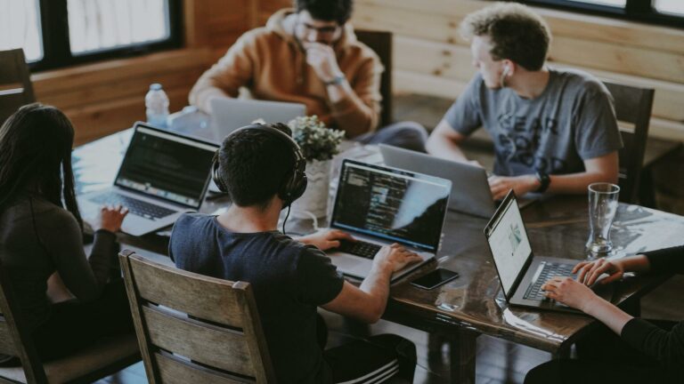 Group of people working on laptops around a table