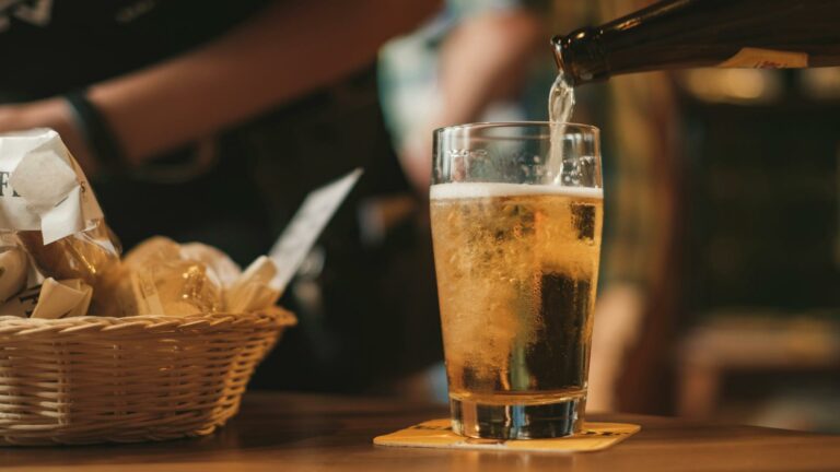 Glass of beer being poured with a basket of snacks nearby