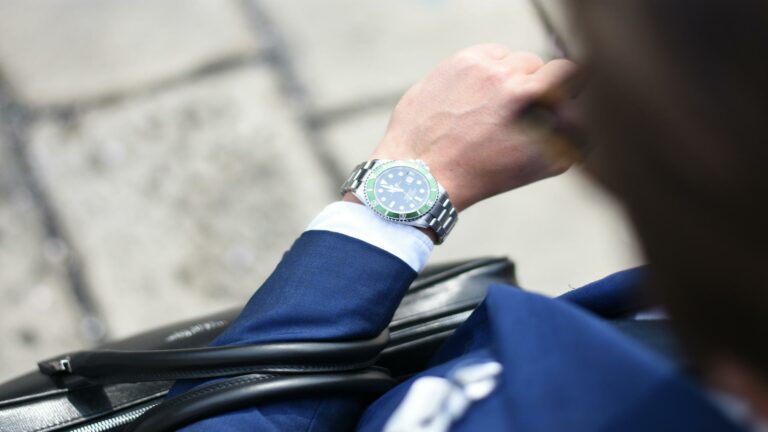 Person wearing navy suit checking time on luxury watch with green bezel while holding leather portfolio