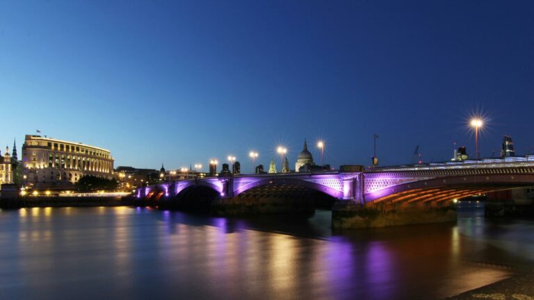 Purple-lit Blackfriars Bridge spanning River Thames at twilight with St Paul's Cathedral and London skyline