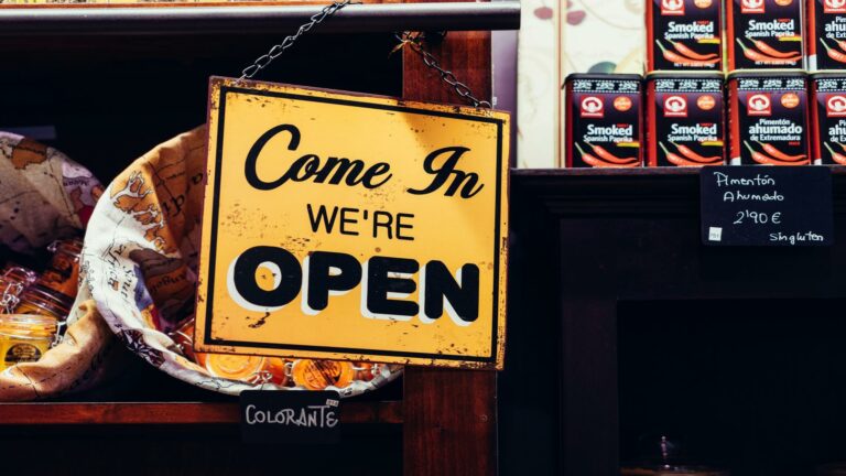 A yellow sign reading 'Come In We're Open' inside a store.