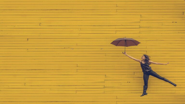 Woman holding an umbrella against a vibrant yellow wooden wall