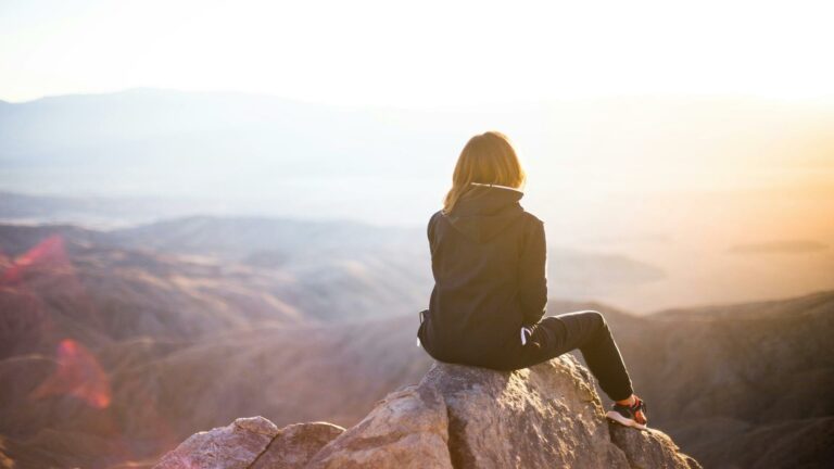 A person sitting on a rock overlooking a scenic mountain view during sunrise.