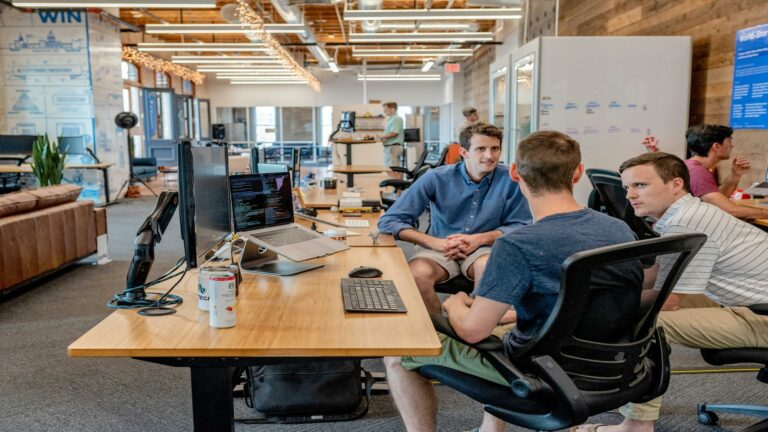 Software developers discussing project in an open-plan startup office with monitors displaying code