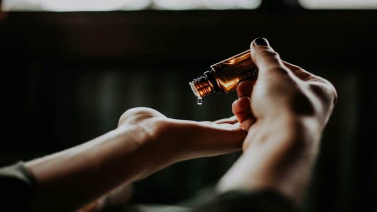 Hand pouring essential oil from a small brown bottle