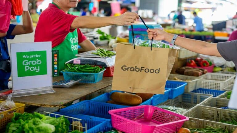 GrabFood delivery bag being handed over at a market stall with GrabPay signage, showcasing a seamless website user interface experience.