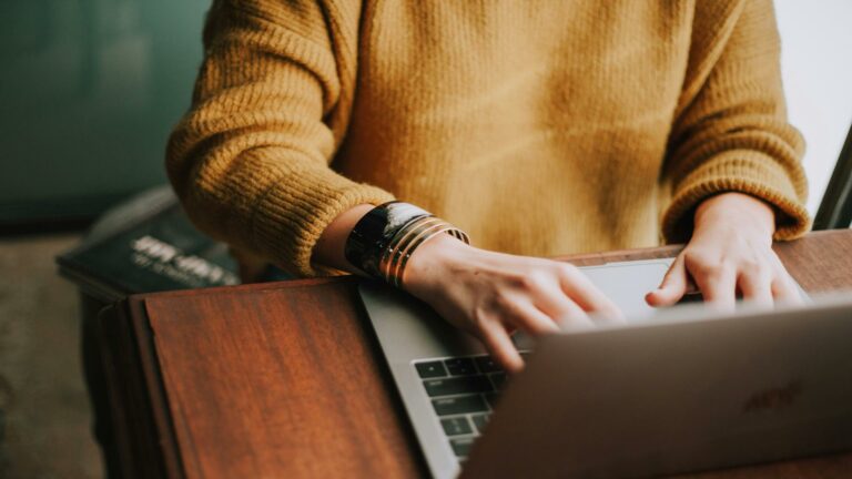 Website design agency professional wearing cozy sweater working on laptop, showcasing modern workspace environment