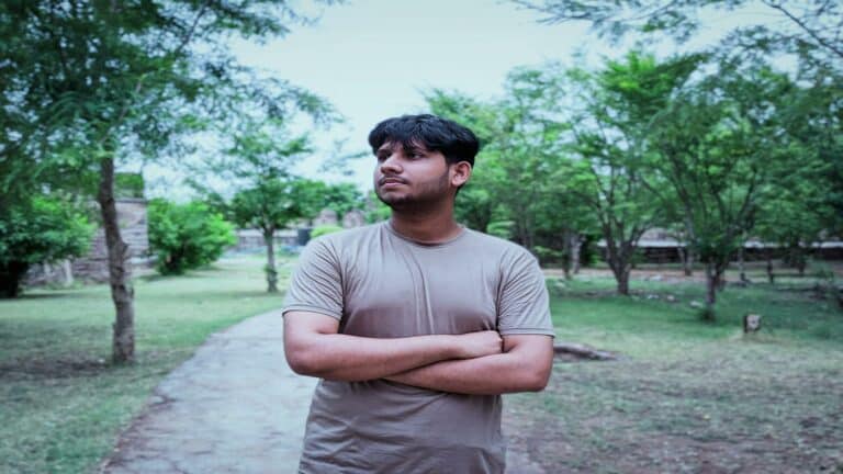 Young professional in beige t-shirt standing confidently with arms crossed in a park setting