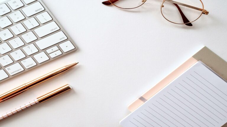 Keyboard, pens, glasses, and notepad on a desk