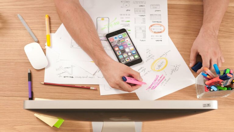 Person working on pay-per-click advertising strategy with notes, a smartphone, and markers on a desk.