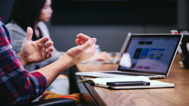 Two people in a meeting discussing SEO strategies with a laptop displaying content on the table.