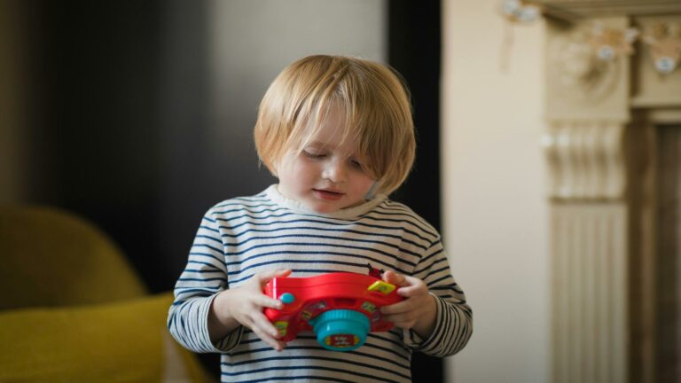 Young child holding and examining a colorful toy camera indoors.