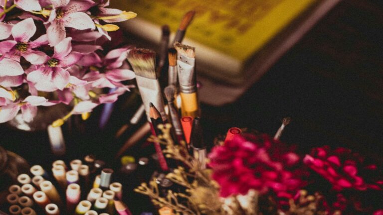 Artistic composition of pink flowers, paintbrushes, and craft materials on a dark background