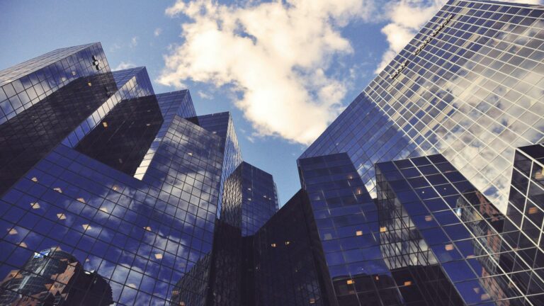 Low angle view of modern glass skyscrapers with reflective surfaces against blue sky with white clouds