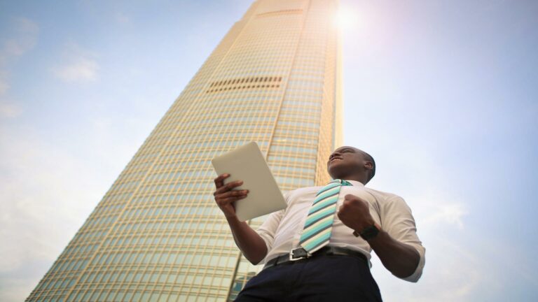 Man holding a tablet in front of a skyscraper