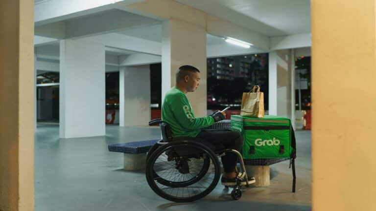 A delivery worker in a wheelchair with a Grab delivery bag.