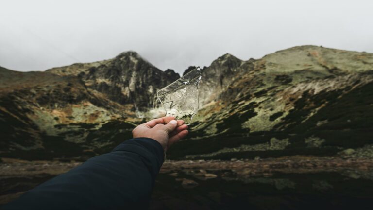 A hand holding a shard of glass with a mountain range in the background.