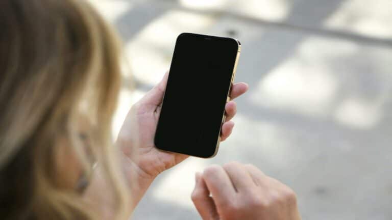 A person holding a smartphone with a blank screen in an outdoor setting.