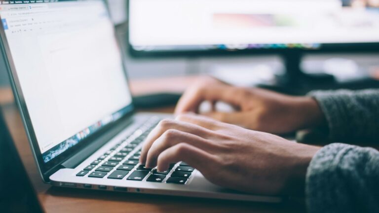 Hands typing on a laptop keyboard with a blurred screen in the background