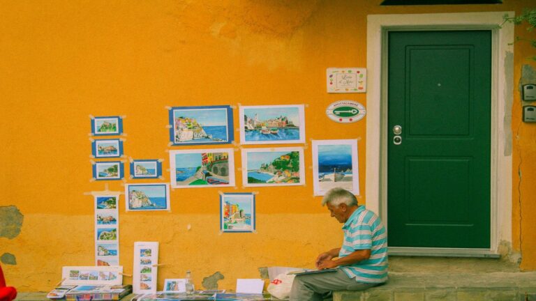 Street vendor displaying coastal artwork against yellow wall with green door