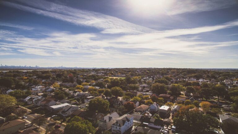 Aerial view of a suburban neighborhood with a distant city skyline under a bright sky