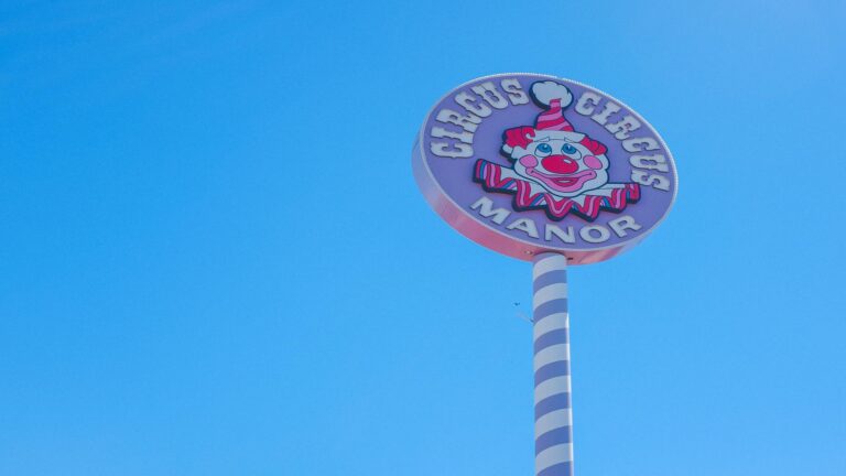 Vintage-style circular sign featuring a clown mascot for Circus Circus Manor against a clear blue sky