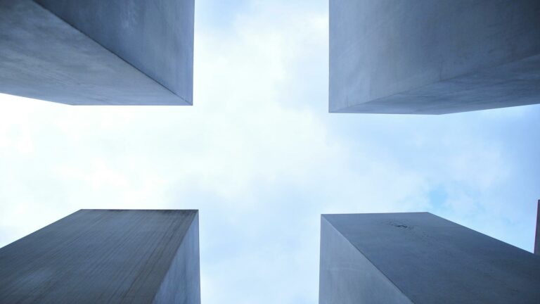 Upward view of four concrete pillars against blue sky creating symmetrical geometric pattern