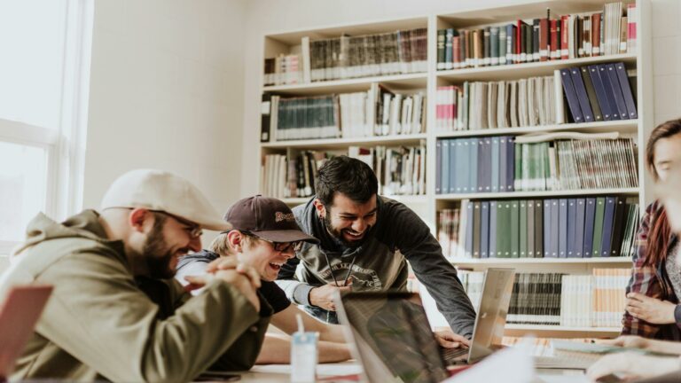 Group of people collaborating and laughing while working on a laptop in a library setting.