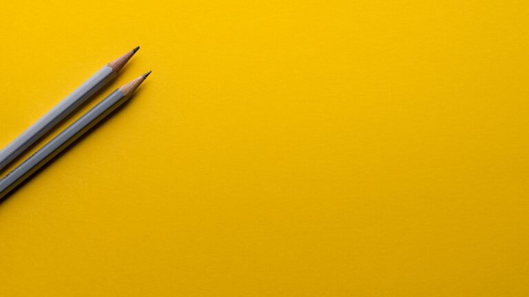 Two sharpened gray pencils placed diagonally on a vibrant yellow surface.