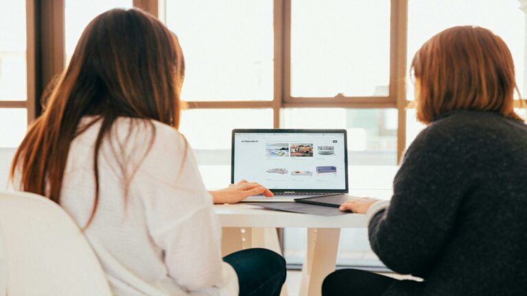 Two women collaborating while viewing content on a laptop screen