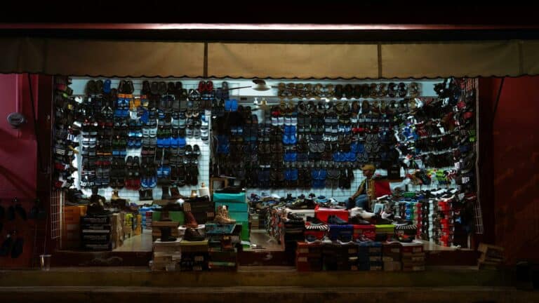 Large retail display of various athletic and casual shoes arranged on a wall with multiple rows of footwear and shoe boxes stacked below