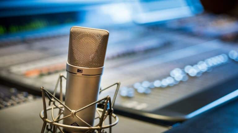 Close-up of a gold condenser microphone with shock mount in a recording studio environment with mixing console in background