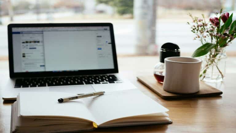 Open laptop and notebook on a desk with coffee and flowers