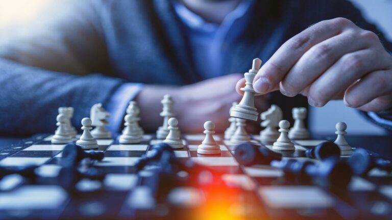 Close-up of hands moving white chess pieces on a chessboard with dramatic blue lighting and orange glow