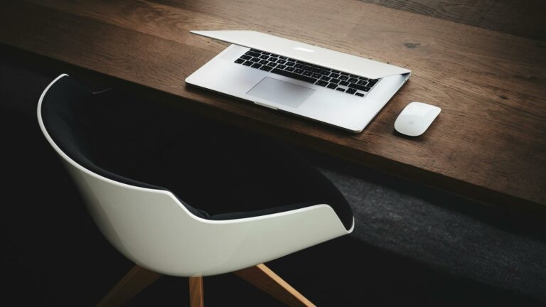 Laptop and mouse on a wooden desk with a chair