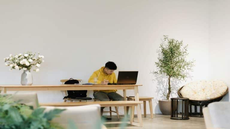 Person in yellow hoodie working on a laptop at a wooden table